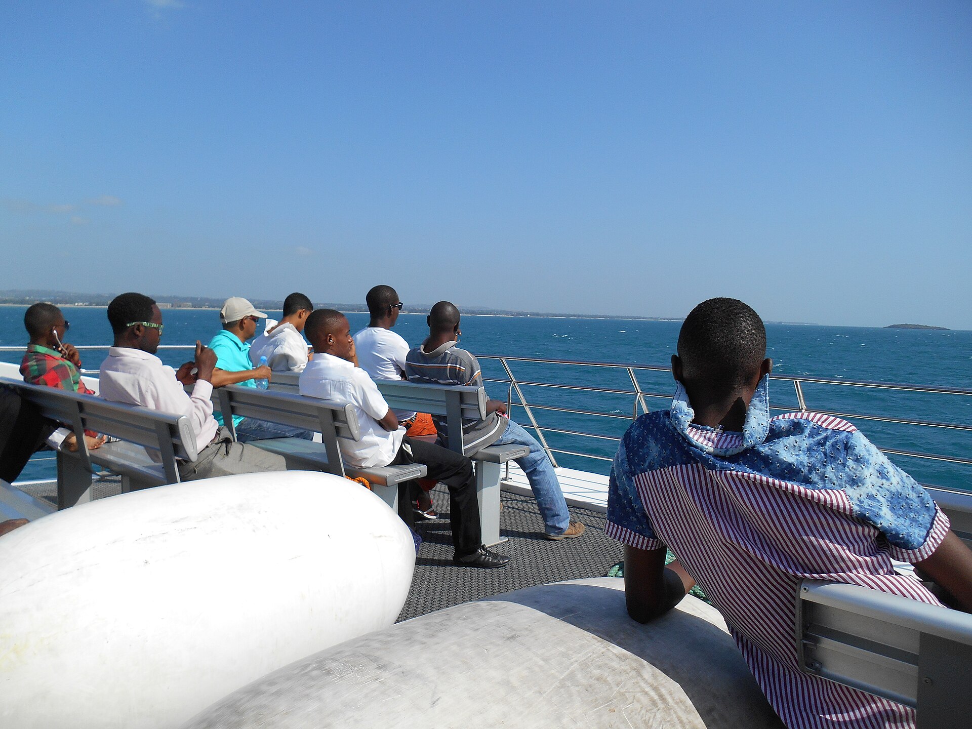 Passengers standing on the open top deck of a ferry from Dar es Salaam to Zanzibar